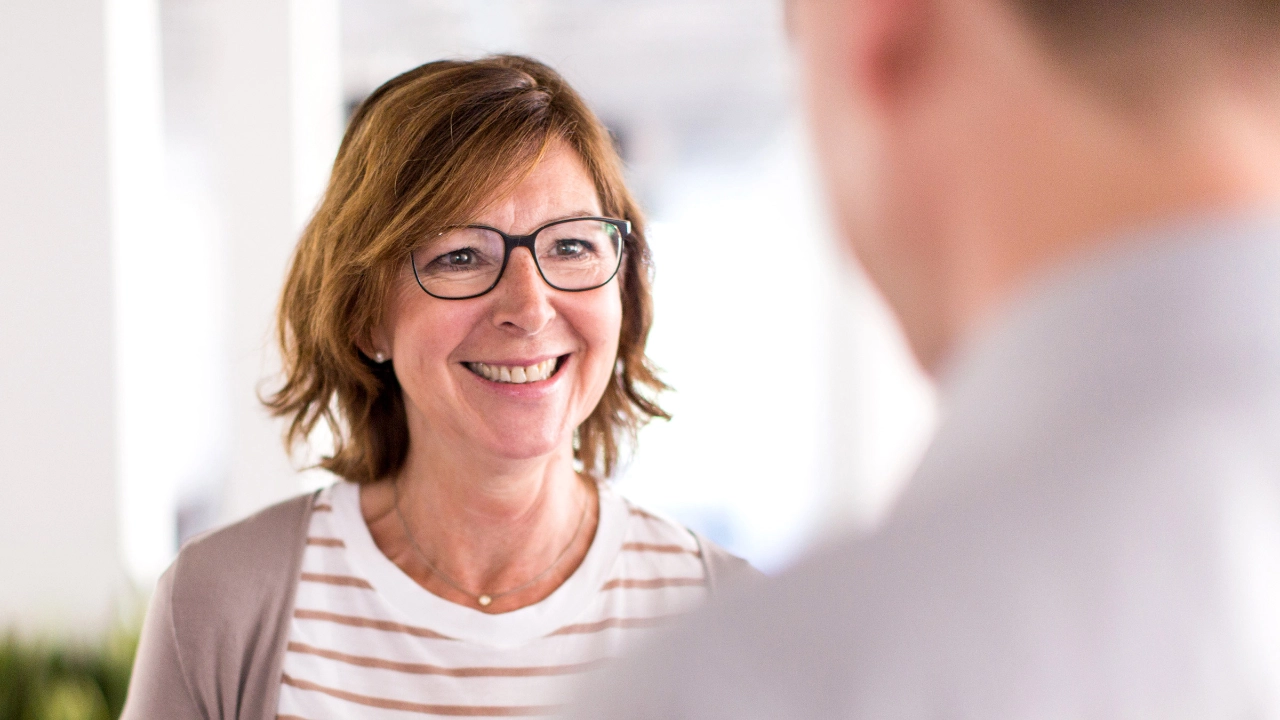 Lächelnde Frau im Gespräch mit einem Mann, der mit dem Rücken zur Kamera steht.