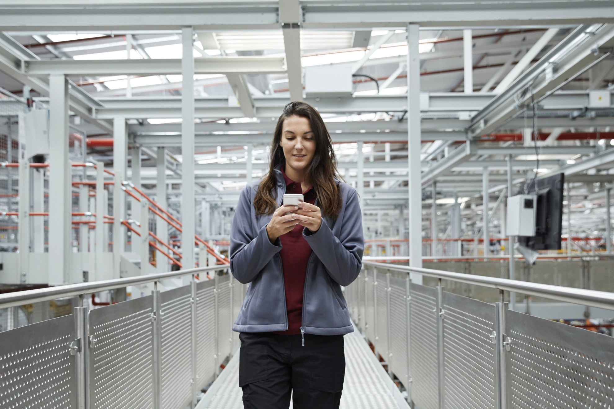 Eine junge Frau in Arbeitskleidung blickt auf ein Smartphone.